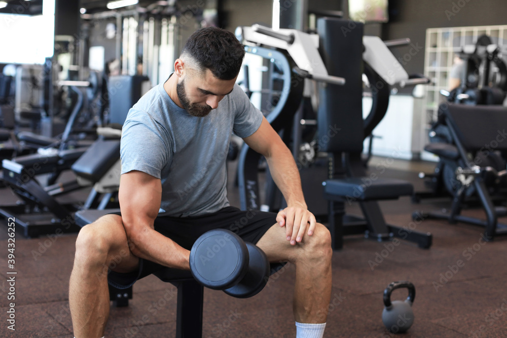 Fit and muscular man doing biceps workouts with dumbbells in gym, copy space. Fit and muscular man doing biceps workouts with dumbbells in gym, copy space.