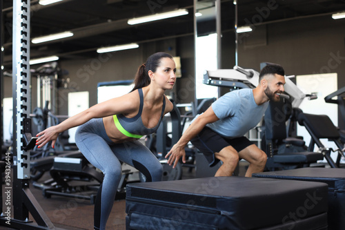 Fit couple doing jumping squats in crossfit gym.