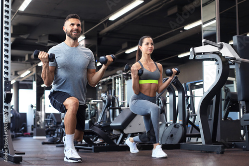 Attractive sports people are working out with dumbbells at gym.