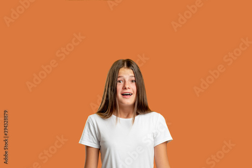 Scared child. Problem anxiety. Panic attack. Shocking news. Portrait of overwhelmed confused teen girl with open mouth in white t-shirt looking at camera isolated on red orange empty space background. photo