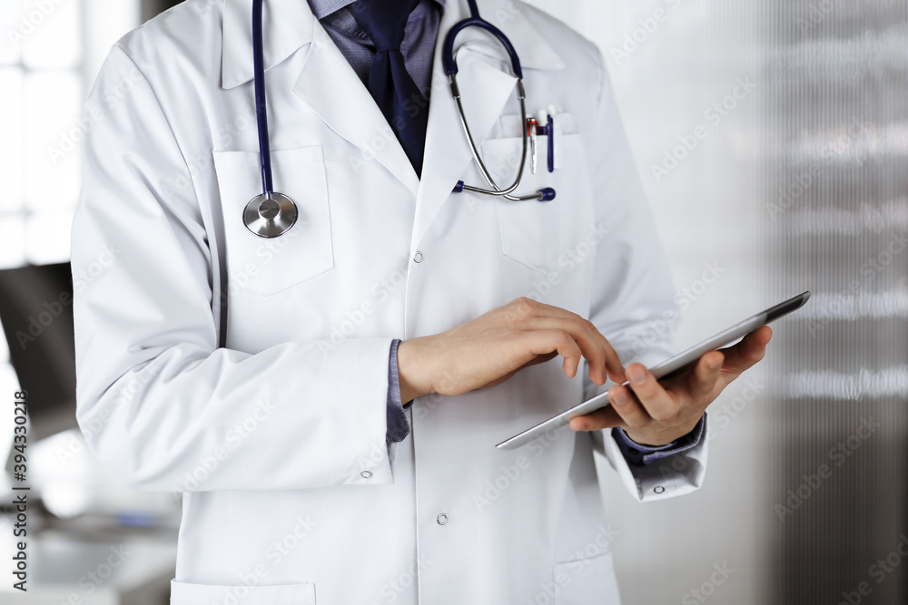 Unknown male doctor using tablet computer in clinic near his working place, closeup. Perfect medical service in hospital. Medicine and healthcare concept Unknown male doctor using tablet computer in clinic near his working place, closeup. Perfect medical service in hospital. Medicine and healthcare concept
