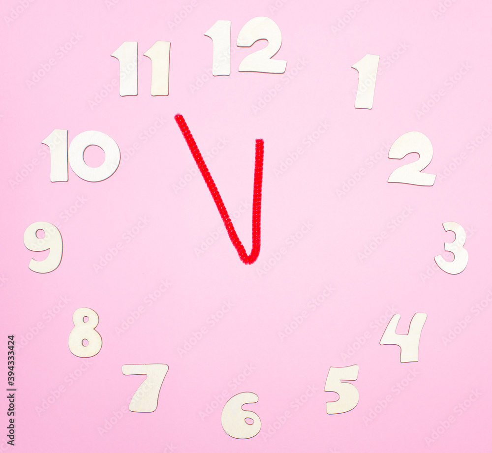 Сlock made of wooden letters arranged in a circle on a pink background. The time is eleven fifty-five. Concept of time, starting new day, starting new year. Сlock made of wooden letters arranged in a circle on a pink background. The time is eleven fifty-five. Concept of time, starting new day, starting new year.