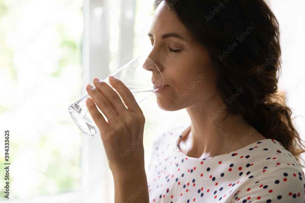Dehydrated young Caucasian woman feel thirsty enjoy clean still mineral water from glass at home. Millennial female drink clear beverage aqua for body refreshment. Hydration, healthy habit concept. Dehydrated young Caucasian woman feel thirsty enjoy clean still mineral water from glass at home. Millennial female drink clear beverage aqua for body refreshment. Hydration, healthy habit concept.