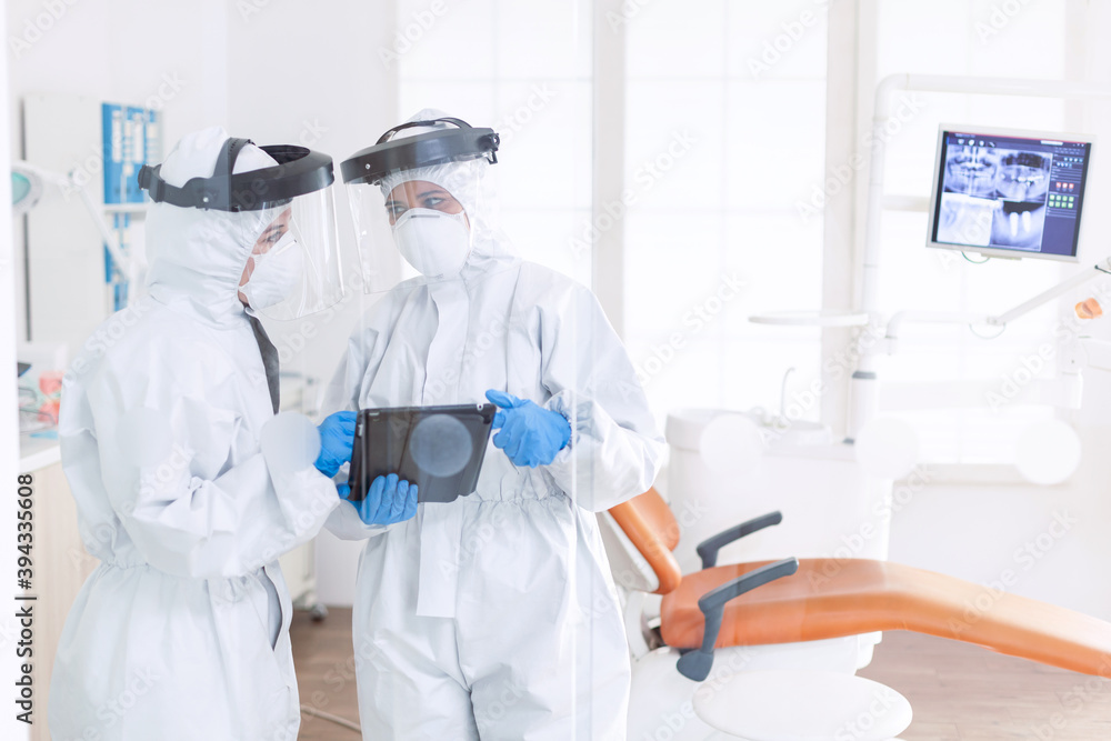 Stomatologs wearing ppe suit discussing patient diagnosis during covid-19. Stomatology team in dental office wearing protective suit agasint contagious coronavirus during global pandemic. Stomatologs wearing ppe suit discussing patient diagnosis during covid-19. Stomatology team in dental office wearing protective suit agasint contagious coronavirus during global pandemic.