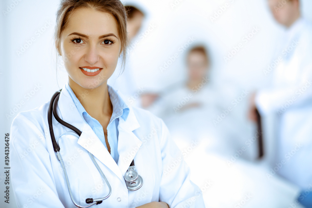 Female doctor smiling on the background with patient in the bed and two doctors Female doctor smiling on the background with patient in the bed and two doctors