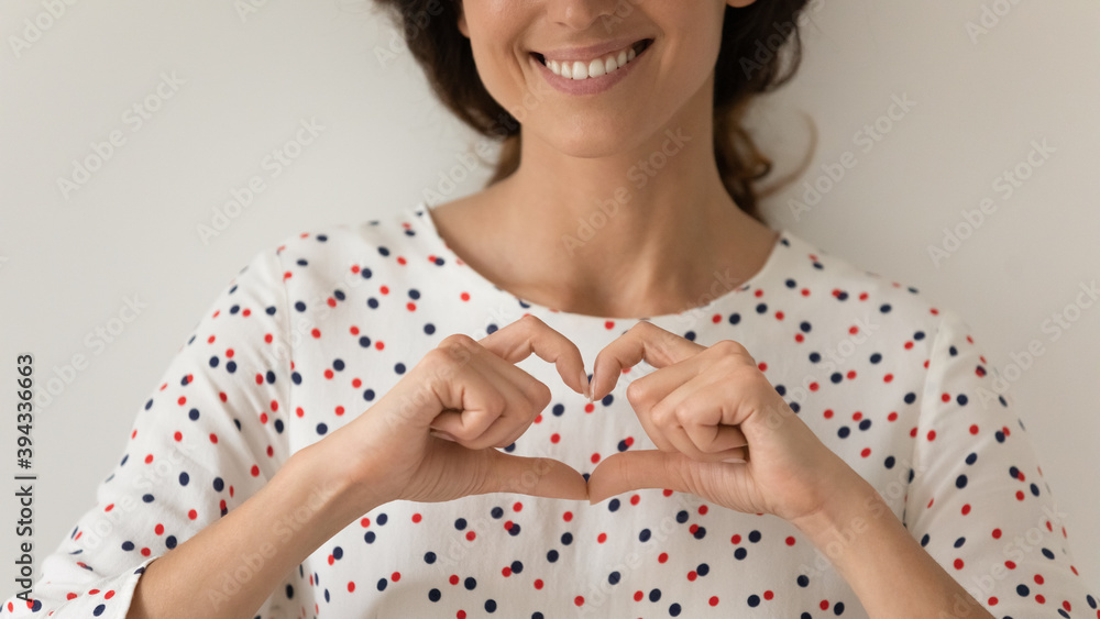 Crop close up of smiling young Caucasian woman isolated on grey studio wall background show heart love hand gesture feeling grateful thankful. Happy female volunteer demonstrate support and care. Crop close up of smiling young Caucasian woman isolated on grey studio wall background show heart love hand gesture feeling grateful thankful. Happy female volunteer demonstrate support and care.
