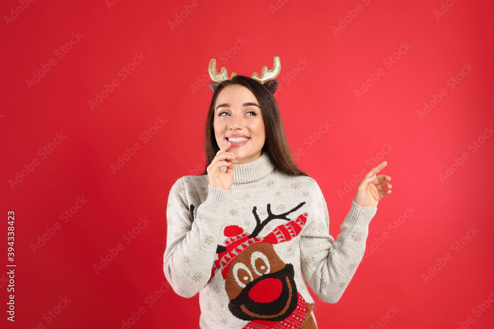Young woman in Christmas sweater and deer headband on red background Young woman in Christmas sweater and deer headband on red background