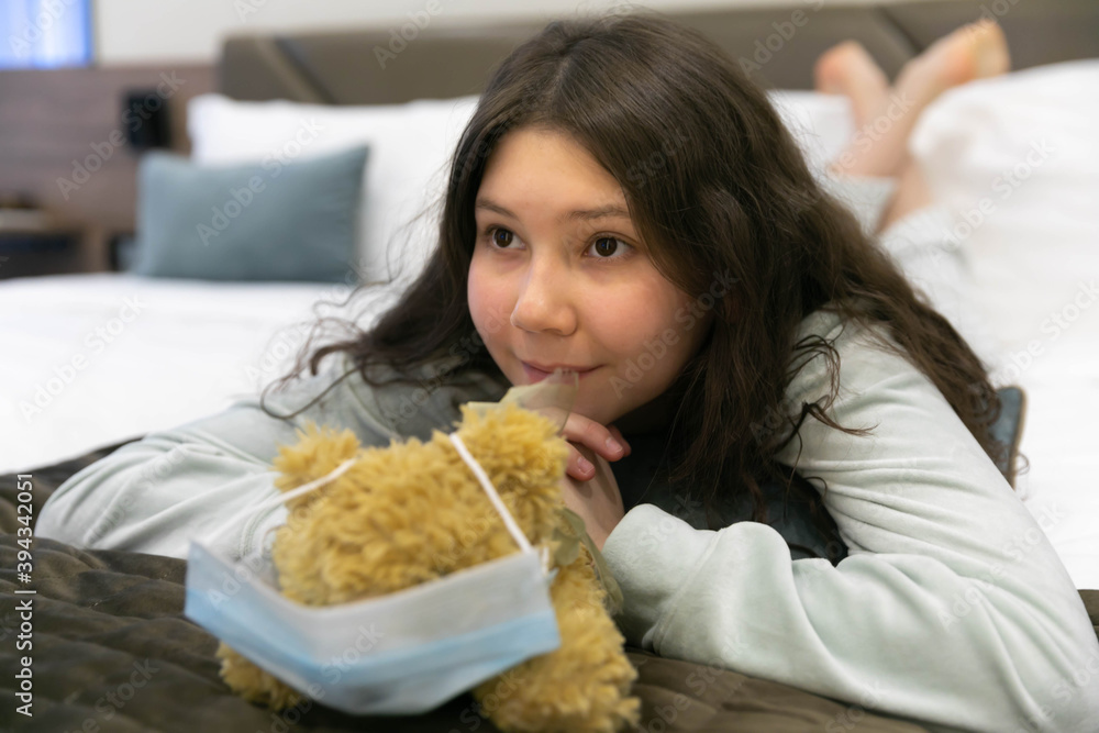 A girl with a Teddy bear wearing a mask against covid, with her favorite toy on Sunday morning in bed is very happy A girl with a Teddy bear wearing a mask against covid, with her favorite toy on Sunday morning in bed is very happy