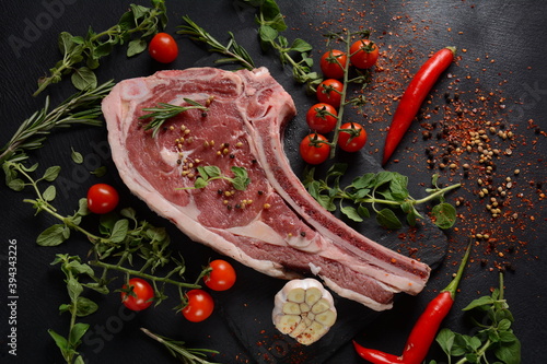 Fresh Raw Beef bone rib steak on black board with herbs and spices