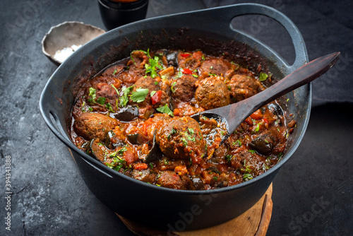 Traditional slow cooked American Tex Mex meatballs with eggplant and mincemeat in a spicy sauce offered as close-up in a design cast-iron roasting dish