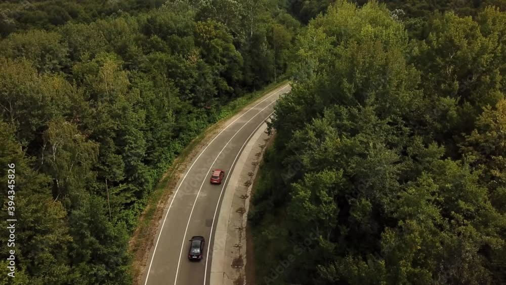 Orange SUV car driving on a rural road in the mountains and forest at summer sunny day - Drone point track view. Orange SUV car driving on a rural road in the mountains and forest at summer sunny day - Drone point track view.