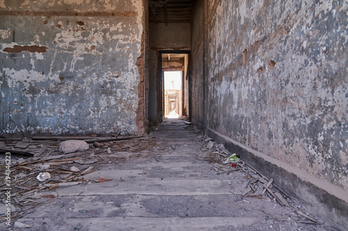 Fototapeta Naklejka Na Ścianę i Meble -  details of the ruins of an abandoned ghost town looking down the hallway, with bright sunlight at the end of it, Chile, South America