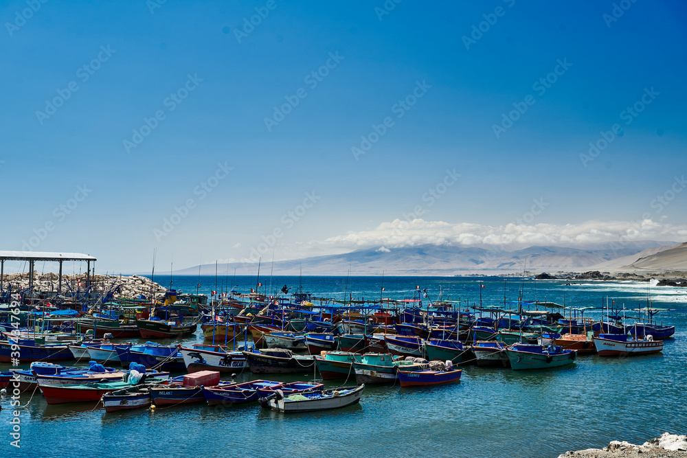 fishing village at the coastline of Peru, a place were desert meets the ocean. Showing blue sky, clouds and a sandy desert beach, fishing huts and boats