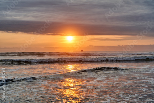 romantic sun set over the pacific ocean at a beach on the coast of Peru with dramatic sky during the golden hour with the silhouette of a ship in the background