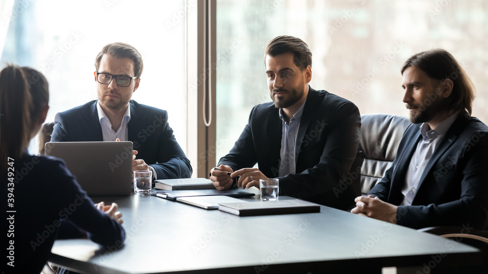 Fototapeta premium Wide panoramic view of employers listen to female job candidate speak at interview in office. Male recruiters have recruitment talk with business partner or client at meeting. Employment concept.