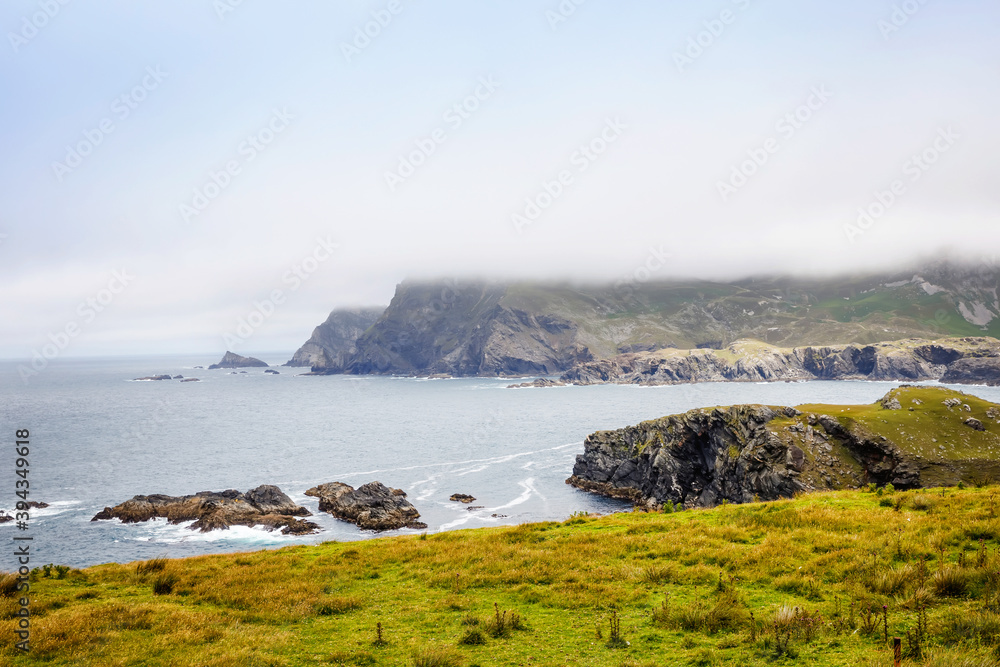 Rugged landscape at Malin Head, County Donegal, Ireland. Beach with cliffs, green rocky land with sheep on foggy cloudy day. Wild Atlantic Way region.