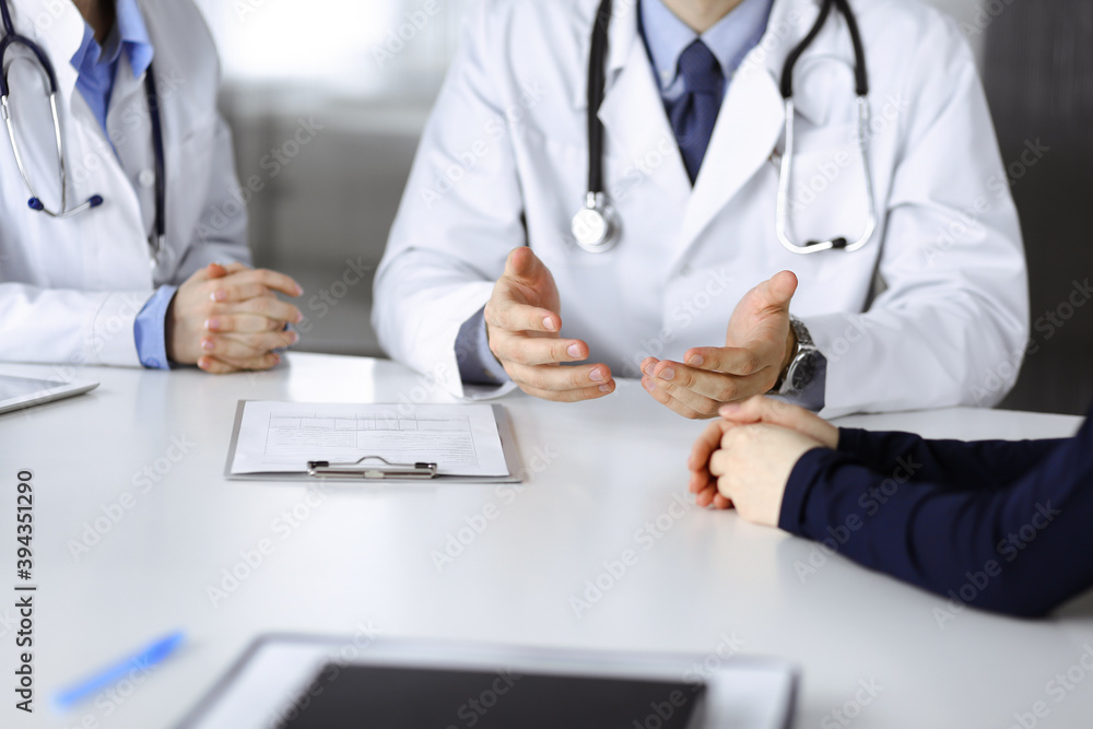 Two doctors and patient woman discussing something while sitting at the desk in modern clinic. Perfect medical service, medicine concept during Coronavirus pandemic. Covid 2019 Two doctors and patient woman discussing something while sitting at the desk in modern clinic. Perfect medical service, medicine concept during Coronavirus pandemic. Covid 2019