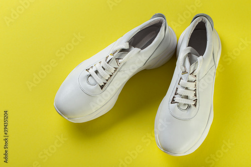 Pair of new white sneakers on yellow background.