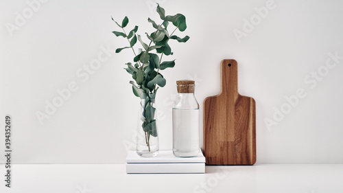 A transparent bottle with a cork stopper  a vase with eucalyptus branches and a wooden board. Natural and eco-friendly materials in interior decor. Copy space  mock up.