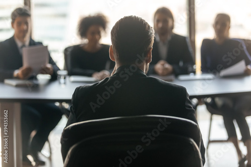 Close up back view of male job candidate apply have interview with employers at office meeting. Man intern or applicant speak on work recruitment talk with company recruiters team. Employment concept.