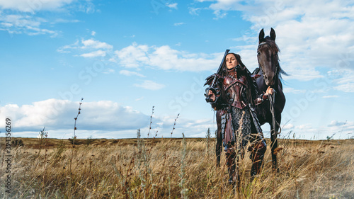 Knight woman in armor with a horse against the sunset fields background