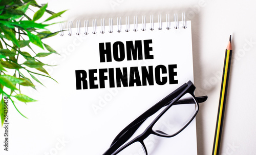 HOME REFINANCE is written in a white notebook next to a pencil, black-framed glasses and a green plant.
