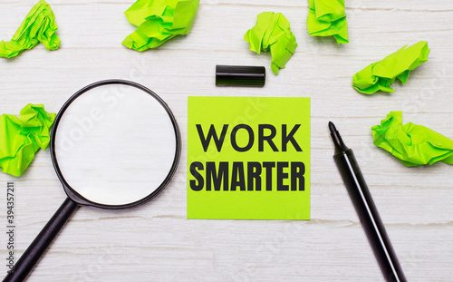 WORK SMARTER written on a green sticky note next to a magnifying glass and a black marker on a wooden table