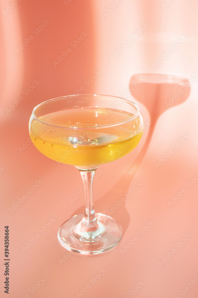 A glass of champagne on a pastel pink background. Bright sunlight, a spectacular long shadow comes from the glass. Creative concept of holiday, celebration, party, alcohol. A glass of champagne on a pastel pink background. Bright sunlight, a spectacular long shadow comes from the glass. Creative concept of holiday, celebration, party, alcohol.
