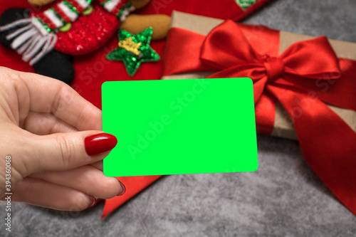 Obraz na plátně The woman's hand holds a white card with a place for text against the background of a gift with a red bow