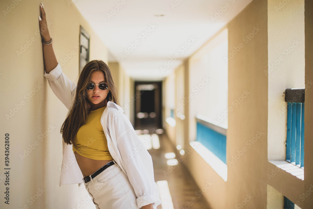 Portrait of beautiful smiling cute tenage model dressed in summer hipster vintage white stylish clothes. Trendy girl posing in the inside background. Funny and positive woman in sunglasses