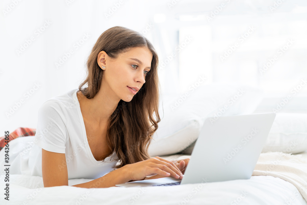 Young woman working at home laying on bed in pajamas, shopping online. Female in bedroom typing on laptop, distance learning for students, surfing Internet in morning after waking up Young woman working at home laying on bed in pajamas, shopping online. Female in bedroom typing on laptop, distance learning for students, surfing Internet in morning after waking up
