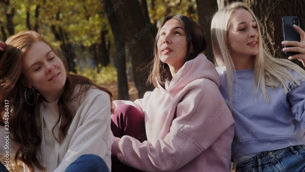 Happy women friends relax in autumn forest. Woman record video on her phone Happy women friends relax in autumn forest. Woman record video on her phone