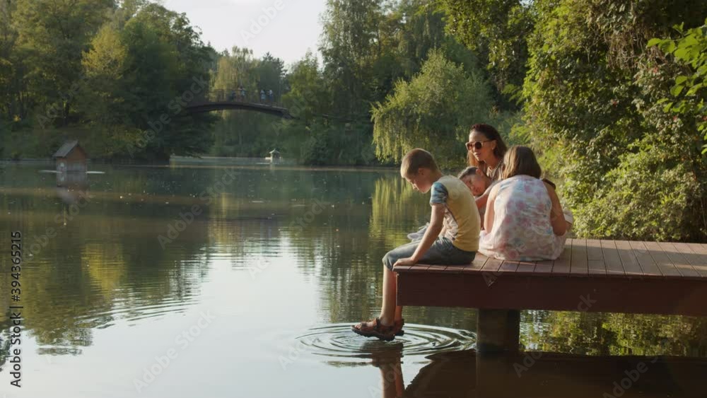 Large multinational family sit on the bridge of the river, lake, pond, sunset, pier, bridge evening, rest Large multinational family sit on the bridge of the river, lake, pond, sunset, pier, bridge evening, rest