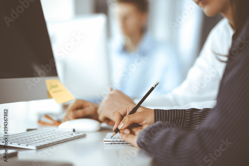 Business woman and man are discussing questions while using computer and blocknote in modern office, close-up. Teamwork in business photo