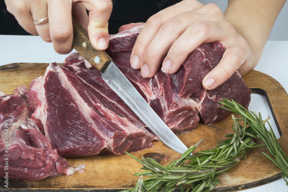 women's hands cut pieces of beautiful red meat with a knife. Cooking meat steaks, chops. pieces of beef meat.