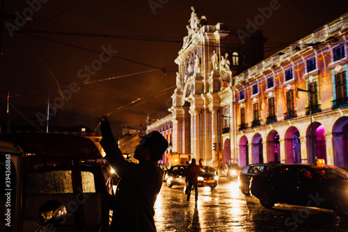 Silhouette of a man in hat taking photos with illuminated Rua Augusta Arch on background during festive Christmas time at night in Lisbon, Portugal