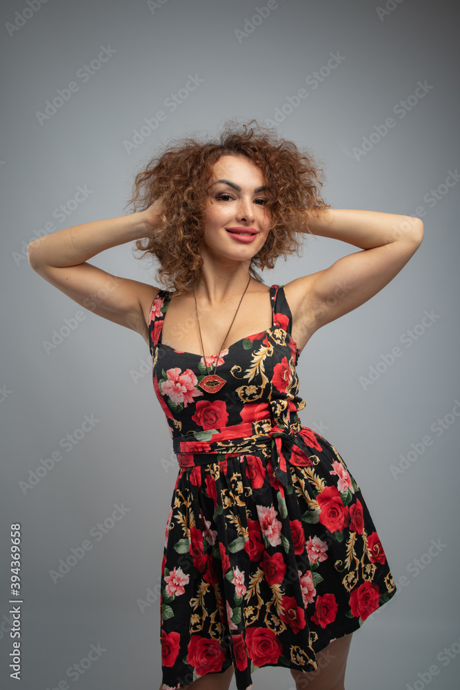 beautiful curly red-haired girl in a black dress with bright flowers on a gray background in a photo studio beautiful curly red-haired girl in a black dress with bright flowers on a gray background in a photo studio