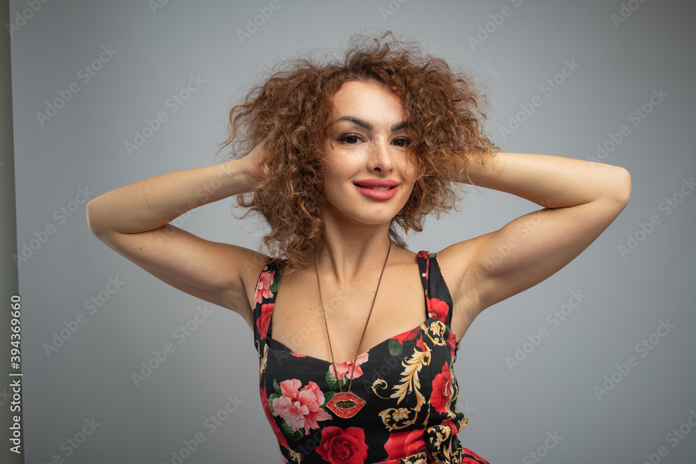 beautiful curly red-haired girl in a black dress with bright flowers on a gray background in a photo studio beautiful curly red-haired girl in a black dress with bright flowers on a gray background in a photo studio
