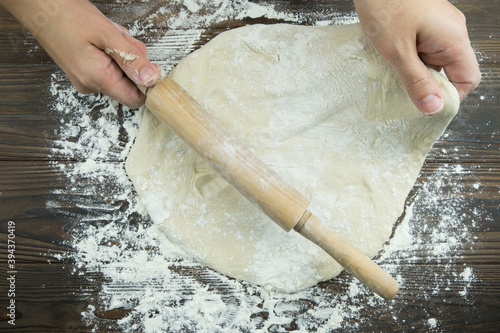 Hands work with the dough to make fresh Italian pasta. Women's hands make dough for homemade pizza on a wooden table strewn with flour . Women's hands roll out the dough