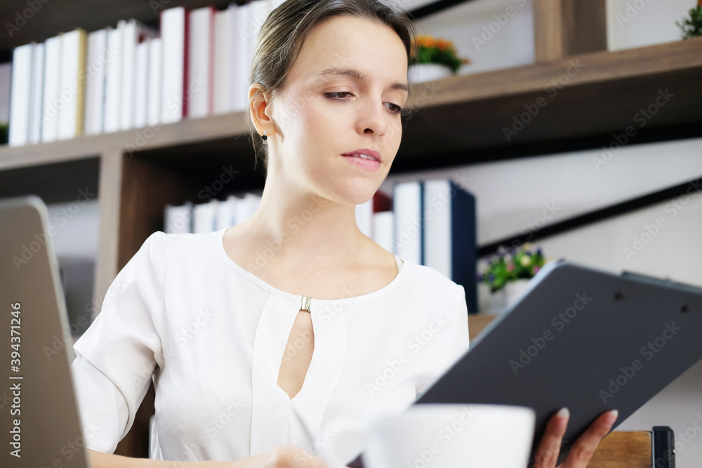 Successful Caucasian young businesswoman is researching on internet with laptop and reading information and knowledge on paper at workplace in office. Technology for Education and business concept. Successful Caucasian young businesswoman is researching on internet with laptop and reading information and knowledge on paper at workplace in office. Technology for Education and business concept.