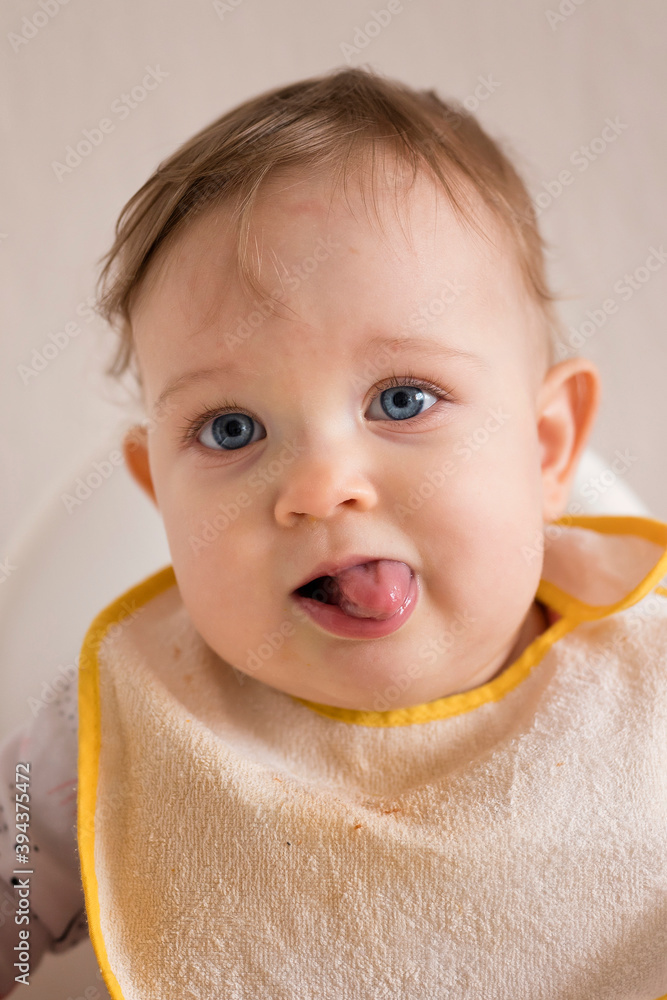 One-year-old girl with her tongue out and a bib in a high chair. One-year-old girl with her tongue out and a bib in a high chair.