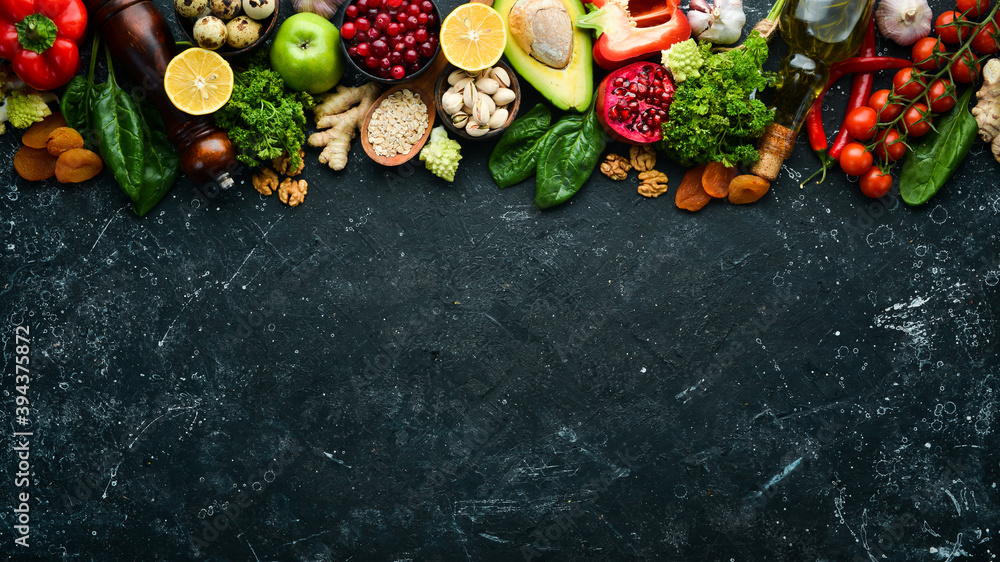 Food background: A set of healthy and clean food - vegetables, fruits, fish, meat, nuts and greens. On a black stone background. Top view. Free copy space.