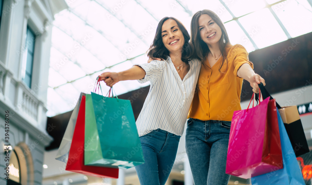Beautiful happy and excited young girl friends with paper bags are walking around the shopping mall Beautiful happy and excited young girl friends with paper bags are walking around the shopping mall