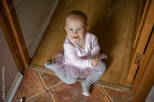 A one-year-old baby in a cute pink dress with a tulle skirt sits on the floor and smiles