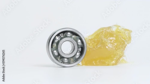 Closed up macro, ball-bearing spin beside yellow lithium grease (NLGI 2) isolated on white background with copy space. Protection of wear and rust. Reduce friction. Engineering and industrial concept