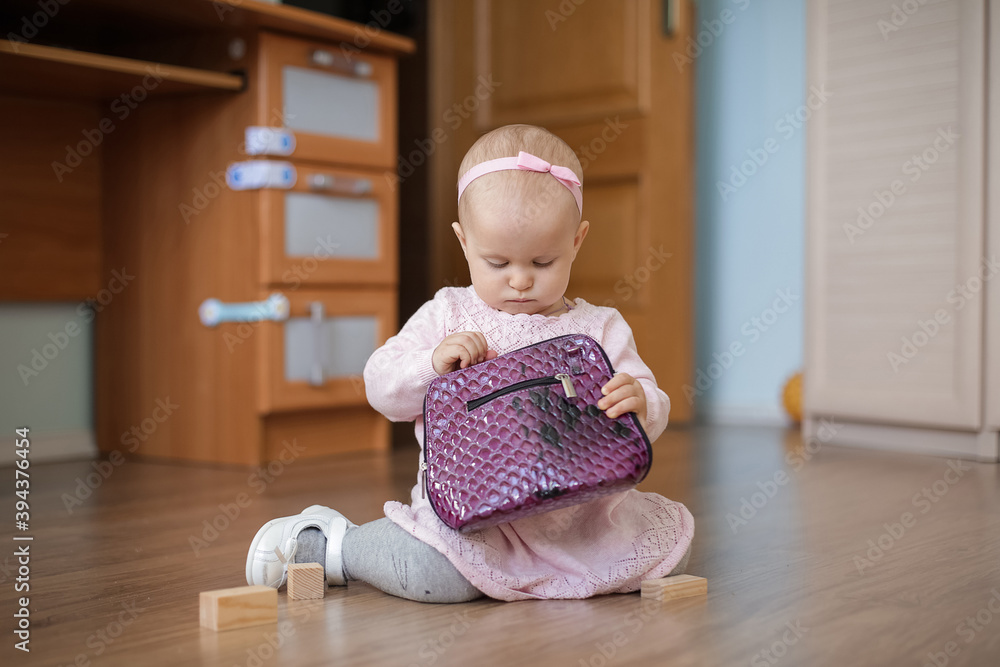 A one-year-old baby in a cute pink dress with a tulle skirt sits on the floor with a purple bag. A one-year-old baby in a cute pink dress with a tulle skirt sits on the floor with a purple bag.