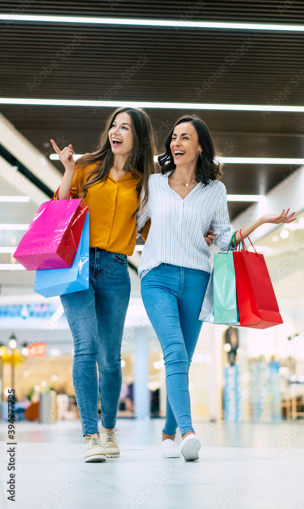 Beautiful happy and excited young girl friends with paper bags are walking around the shopping mall Beautiful happy and excited young girl friends with paper bags are walking around the shopping mall