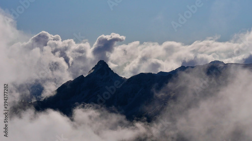 Mystic view of the silhouettes of rugged mountains in the European Alps surrounded by rising clouds above Montafon valley, Austria in autumn season.