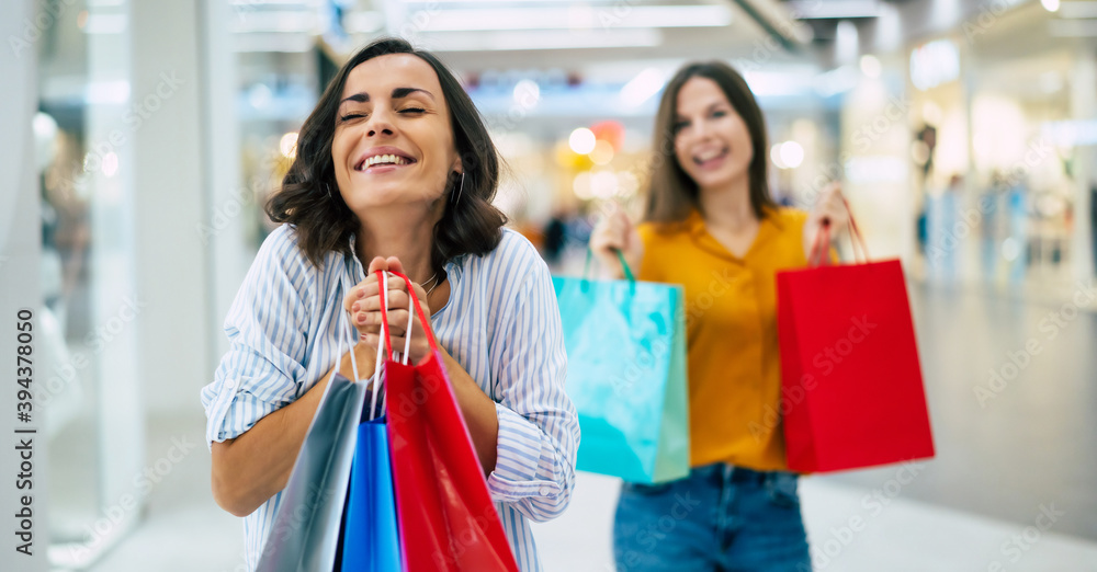 Beautiful happy and excited young girl friends with paper bags are walking around the shopping mall