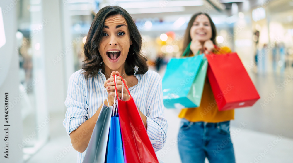 Beautiful happy and excited young girl friends with paper bags are walking around the shopping mall